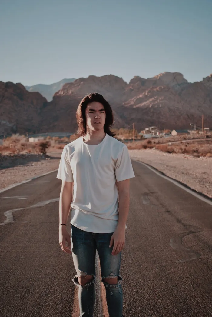 man wearing white tee shirt and tattered jeans standing on road