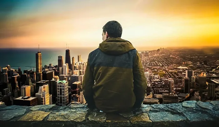 一名男子坐在一座高大的石头平台边缘，俯瞰着一座现代城市。