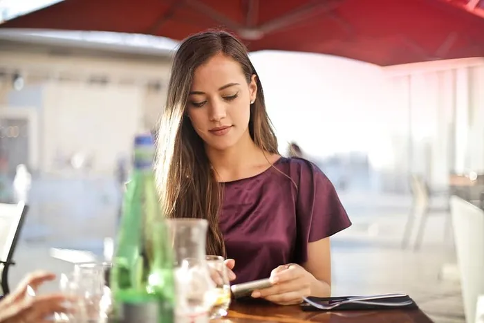 在一家餐厅里，一位身穿紫红色连衣裙的金发女郎看着手机屏幕