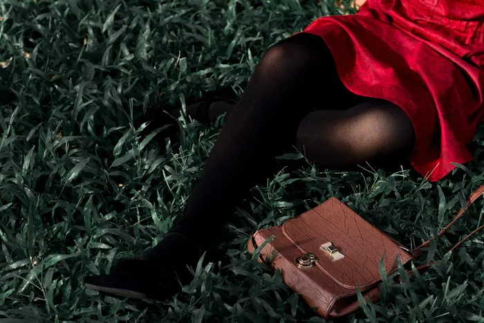 穿着红色连衣裙、穿着黑色长袜的女人坐在草地上