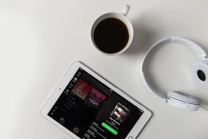 耳机、咖啡和iPad平板电脑，在白色桌面上打开Spotify音乐应用程序
