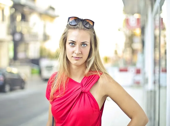 一位身穿红色连衣裙、戴着太阳眼镜的金发女郎在人行道上摆姿势