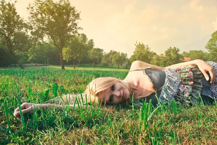 阳光下躺在草地上的穿着意大利面条纹花裙的金发女郎