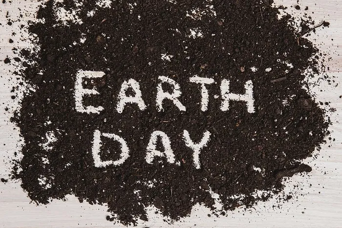 文字“地球日”写在白色木质表面的深色土壤中，传达保护自然资源的信息