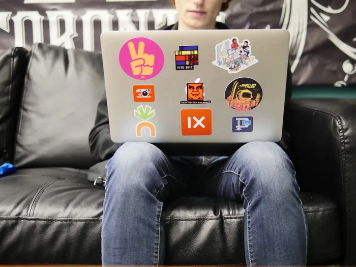 坐在黑色真皮沙发上使用银色MacBook的男子
