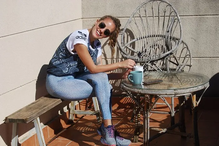 坐在长凳上搅拌咖啡的微笑女孩