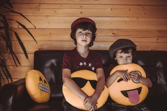 两个男孩拿着表情符号坐在沙发上扔枕头