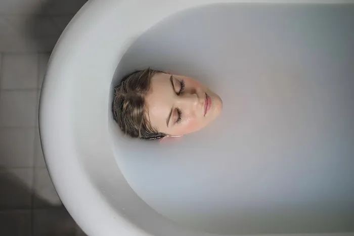 一名女子闭着眼睛躺在乳白色浴缸里的照片