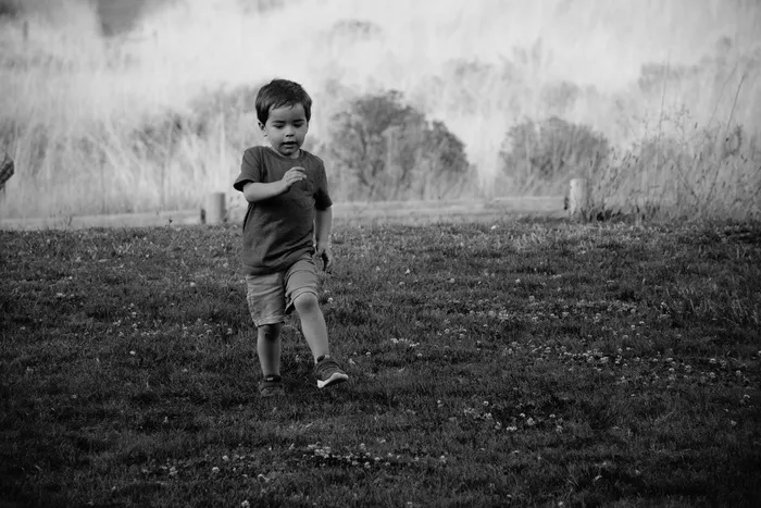 小孩在草地上行走的灰度照片