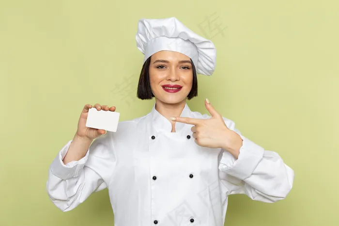 一位年轻的女厨师穿着白色的厨师服，戴着白色的帽子，绿色的墙上挂着微笑的女士工作食品的颜色