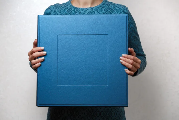 一位女士拿着一本家庭相册，放在时尚设计师的方形盒子里。女性手举方形相册相册盒。女士手中的蓝色大礼盒，靠近文字的复印空间