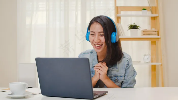 自由职业女性商务休闲服使用笔记本电脑工作电话视频会议与客户在工作在客厅在家。快乐的年轻亚洲女孩坐在办公桌上放松一下上网。