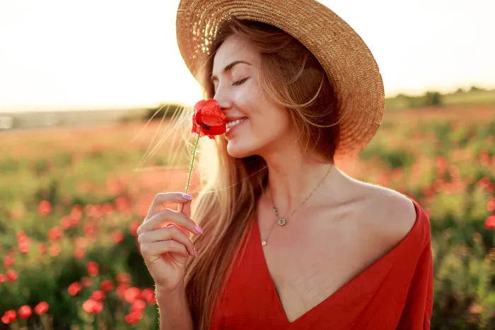 浪漫的金发女人手拿鲜花在神奇的罂粟地散步。暖暖的夕阳色。草帽。红色连衣裙。柔和的颜色。