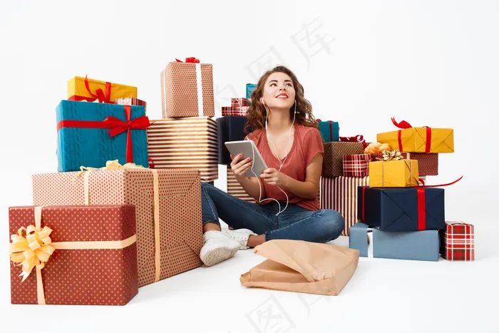 年轻的卷发女人坐在礼品盒中的地板上，手里拿着刚刚打开的礼物板