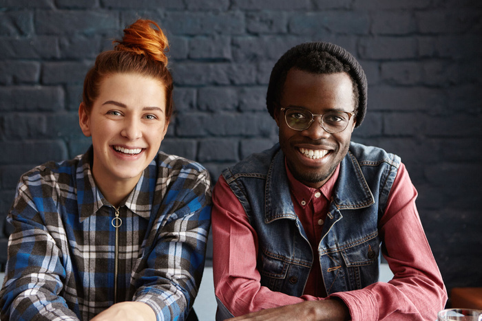 可爱的跨种族夫妇在室内休息靠着黑砖墙坐着