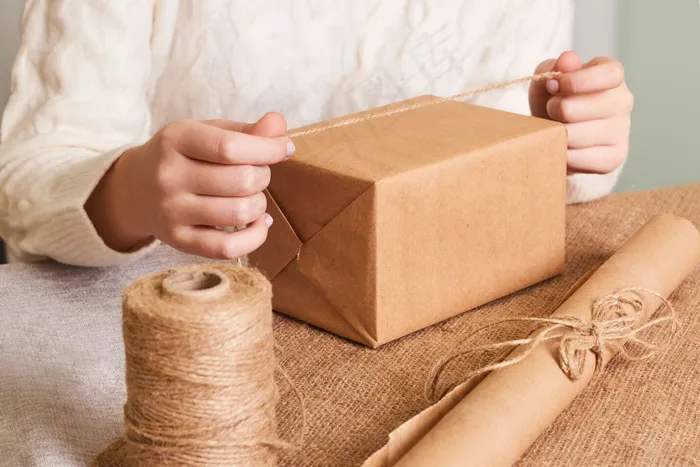 重点放在女人手上的白色针织毛衣包装盒里。手工包装纸和天然绳线。节日礼物，惊喜。节礼日礼物
