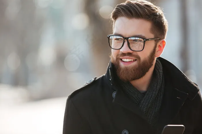 戴着眼镜的快乐胡子年轻人站在户外的肖像