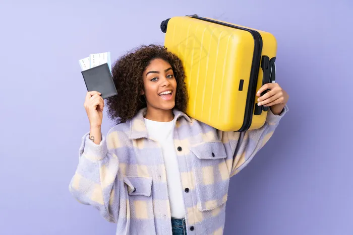 紫色墙上的年轻非洲裔美国妇女带着手提箱和护照在度假