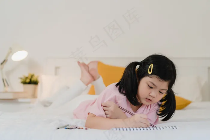 年轻的亚洲女孩在家画画。亚洲日本女人小孩睡前放松休息愉快快乐画漫画躺在床上，晚上在卧室里感受舒适和平静的概念。