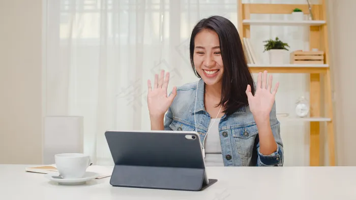 自由职业女性商务休闲服使用平板电脑工作电话视频会议与客户在工作在客厅在家。快乐的年轻亚洲女孩坐在办公桌上放松一下上网。