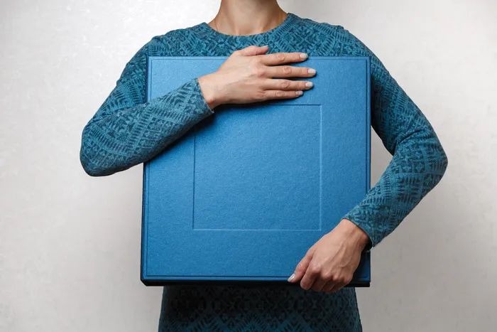 一位女士拿着一本家庭相册，放在时尚设计师的方形盒子里。女性手举方形相册相册盒。女士手中的蓝色大礼盒，靠近文字的复印空间