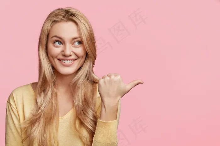 一头金发蓝眼睛的快乐女性的水平肖像，闪着微笑，做一些产品的广告，一边示意，对着粉红色的墙上摆出你的广告文字的复制空间