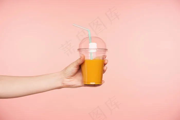 侧视图年轻女子的手被提出，而持有新鲜果汁与吸管在它，隔离在粉红色的背景。餐饮摄影概念